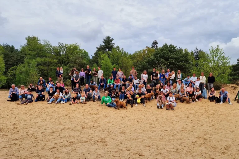 Groepsfoto van eigenaren met hun Australian Labradoodles tijdens een buitenbijeenkomst